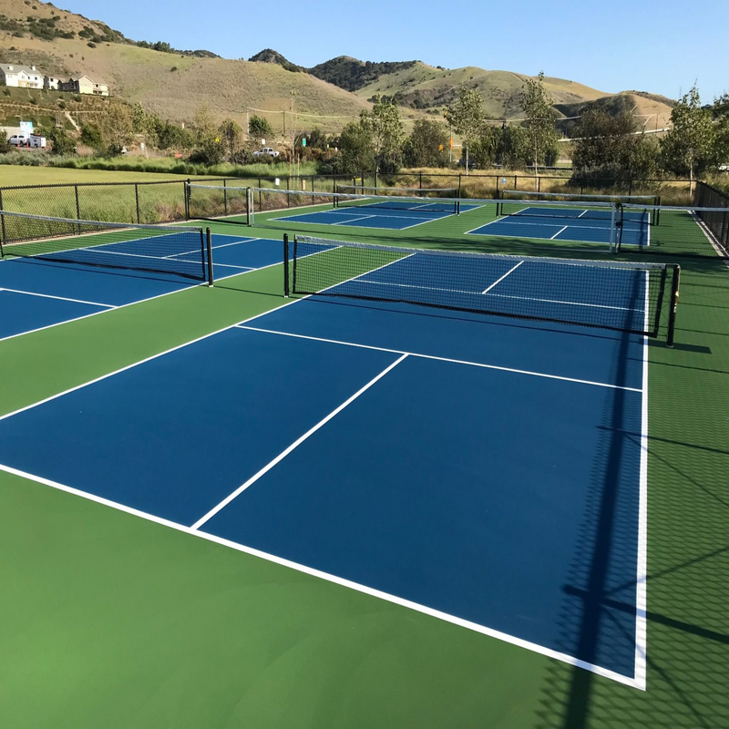 Newly built pickleball court complex with blue-green LDK flooring and regulation nets, ready for play