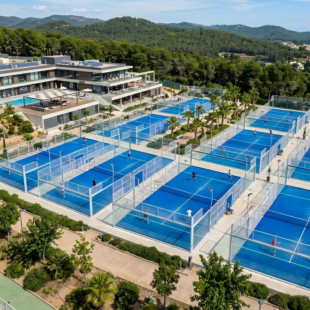 Aerial panoramic view of an outdoor sports club or resort featuring multiple professional blue padel courts.