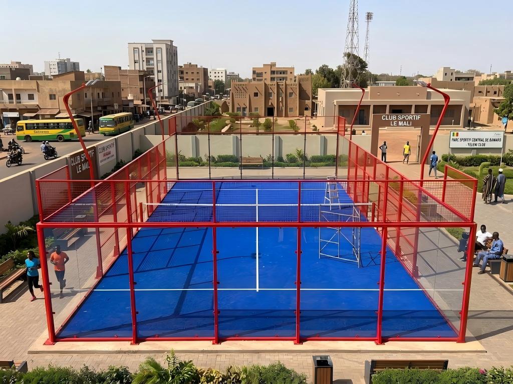 A newly constructed, empty outdoor glass padel court featuring a blue playing surface and red enclosures.