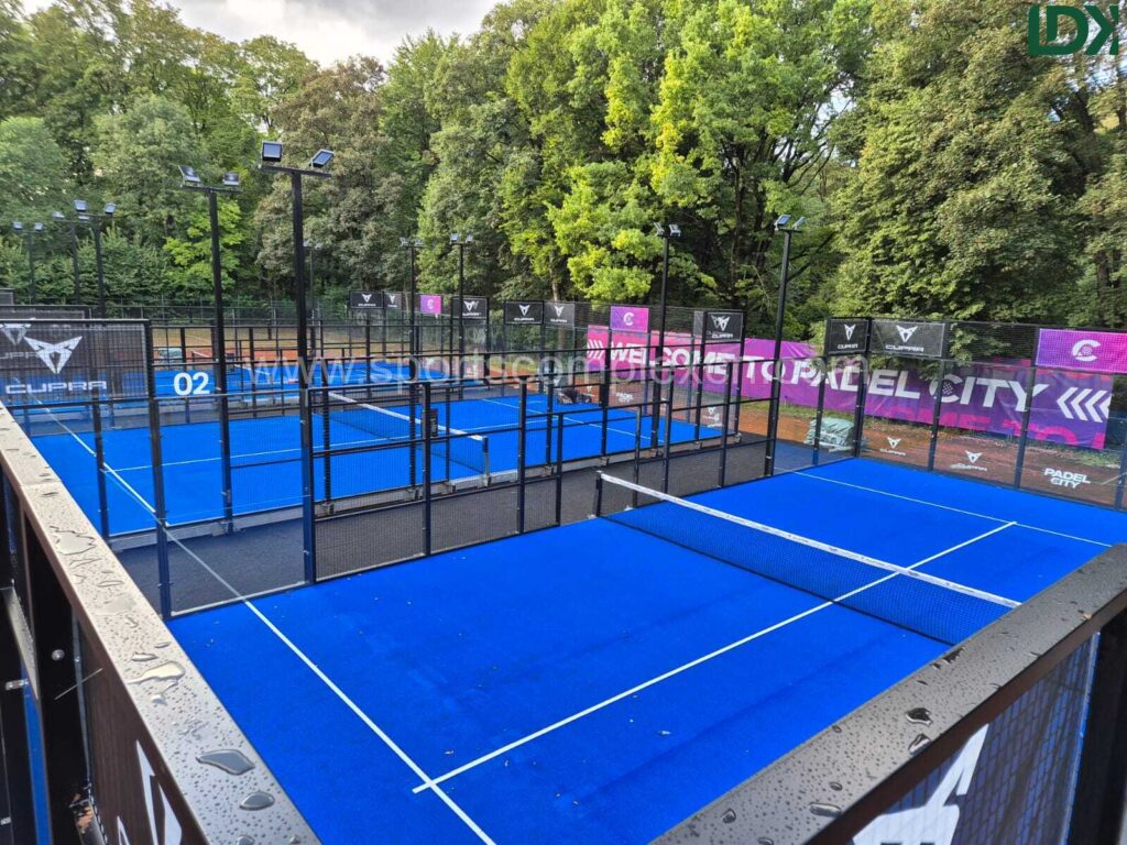 Elevated view of two completed outdoor padel courts side-by-side, featuring bright blue turf and surrounded by trees.