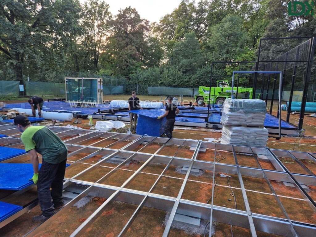 Construction workers assembling the metal base frame grid for a padel court in an outdoor park.