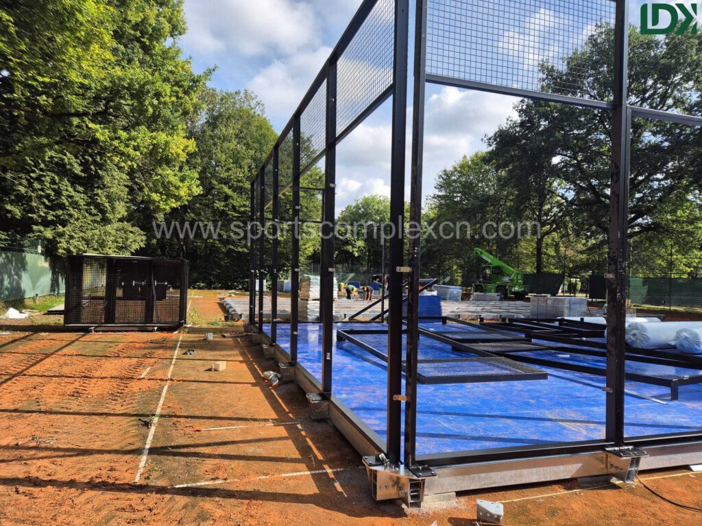 Padel court installation in progress, highlighting the black metal fencing framework and blue playing surface.