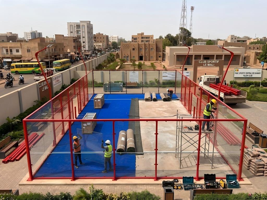 Construction workers building an outdoor padel court with a red frame and blue surface in Mali.