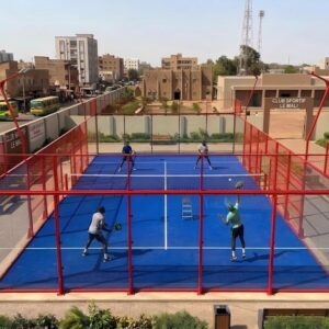 Four people actively playing a match on an outdoor blue glass padel court in Mali.