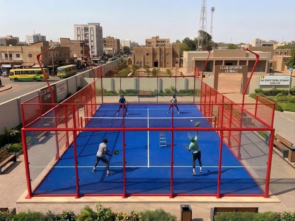 Four people actively playing a match on an outdoor blue glass padel court in Mali.