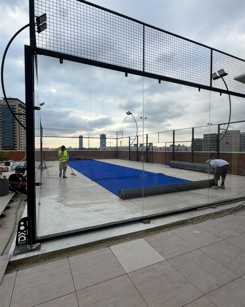 Workers installing the blue playing surface inside the court's glass and mesh enclosure.